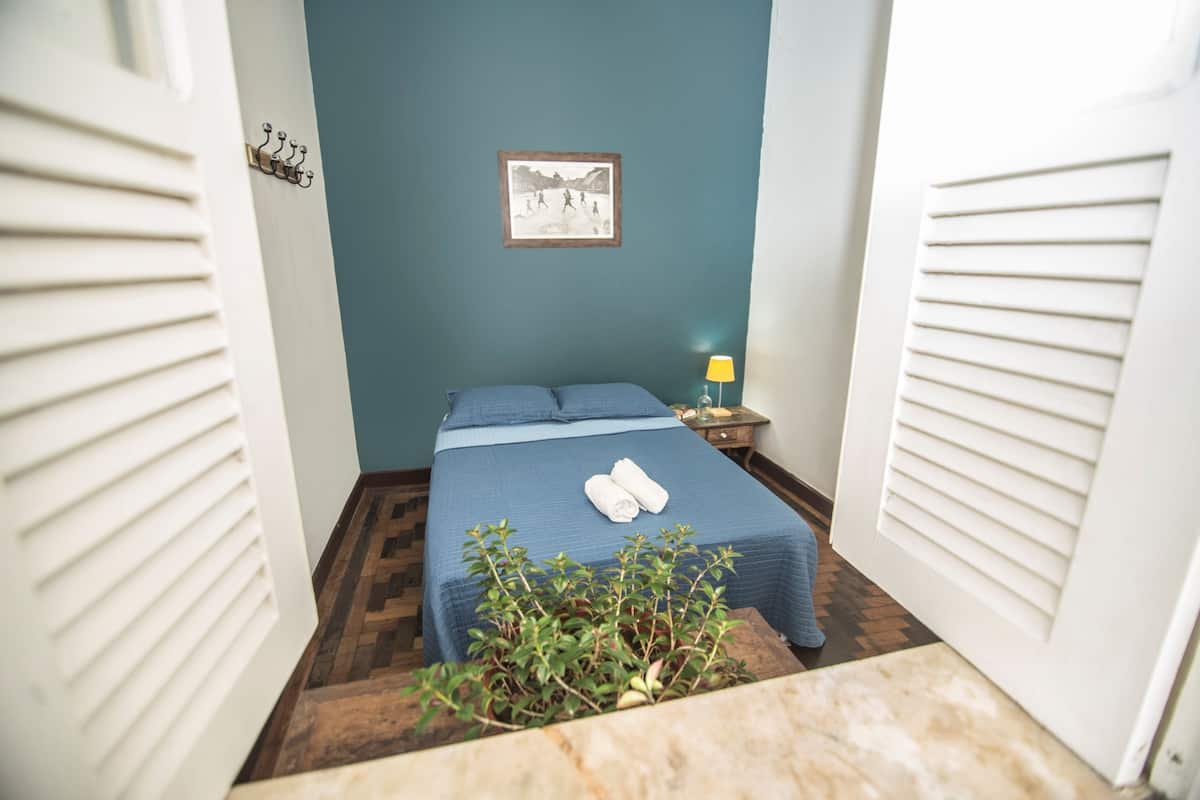 Quarto com cama, mesa de cabeceira, abajur e quadro na parede.