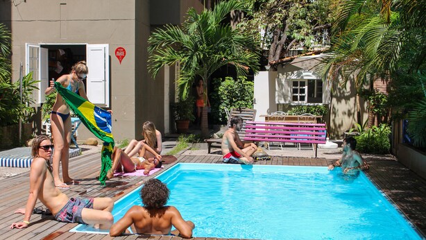 Piscina rodeada por um deck de madeira, com pessoas relaxando e socializando.