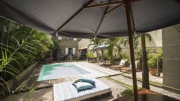 Een achtertuin met een zwembad, een houten terras en een loungehoek met een hangmat.