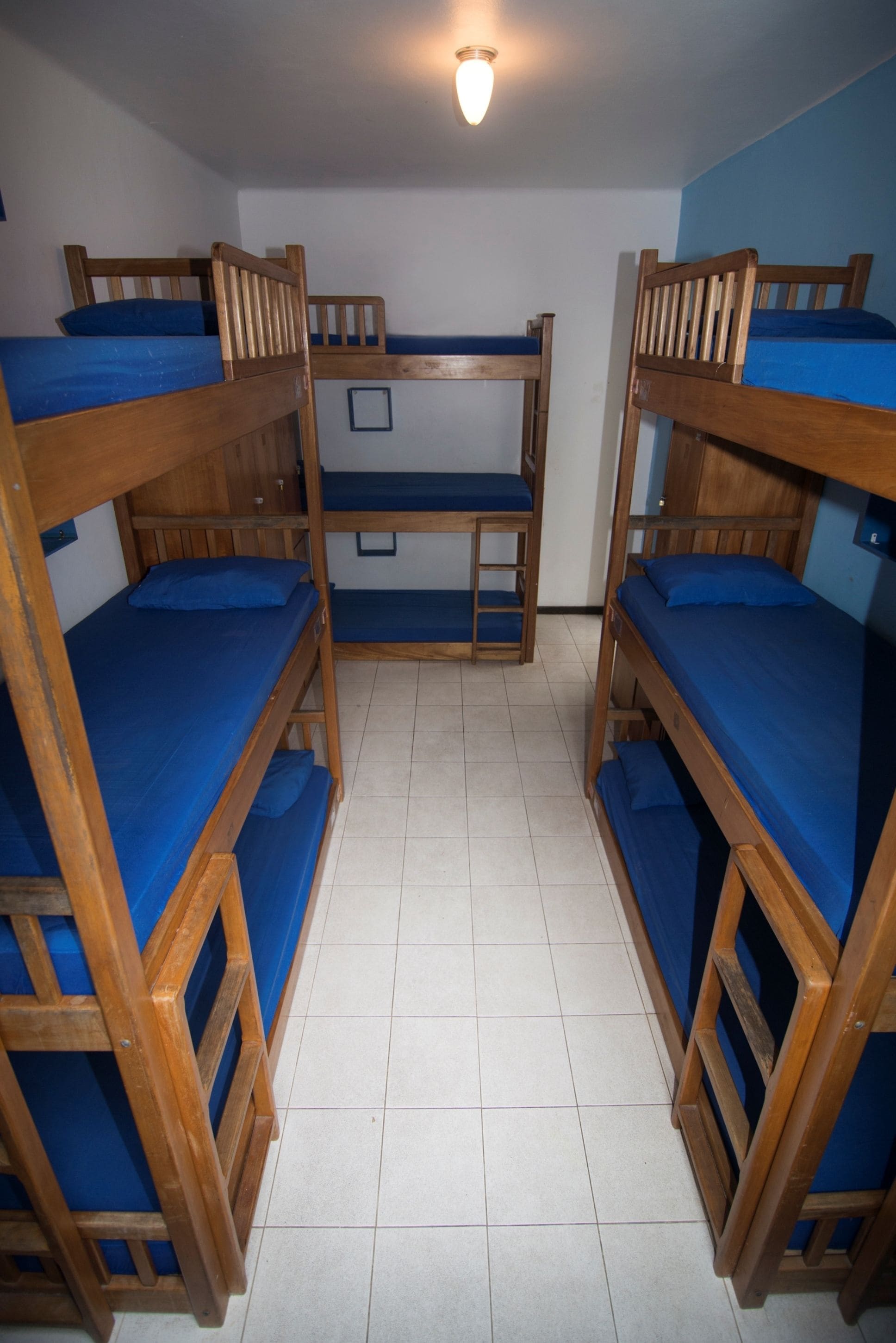 Ein Zimmer mit vier Etagenbetten, jedes mit blauer Matratze und Holzrahmen.