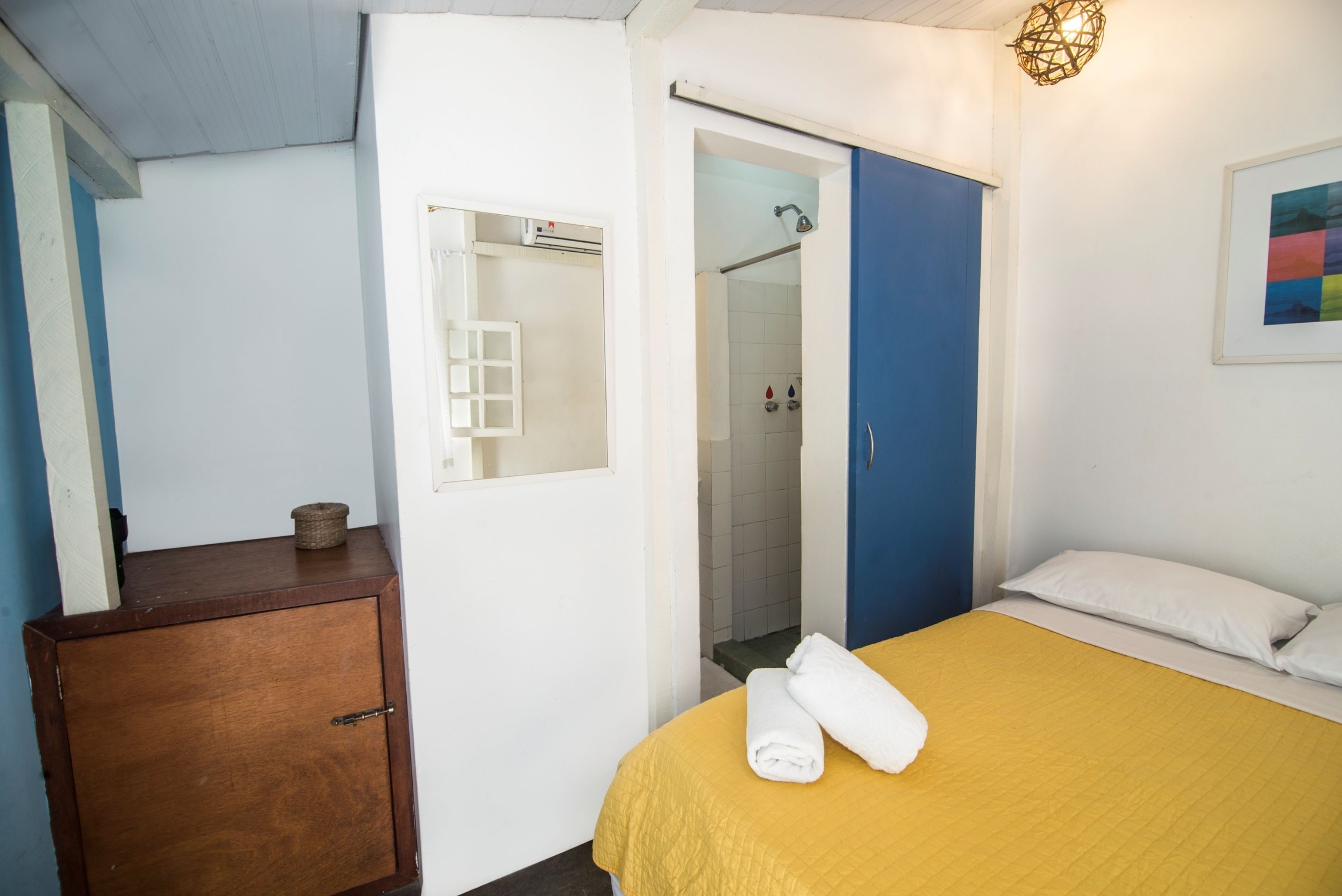Une chambre à coucher avec une couvre-lit jaune, une armoire en bois, une commode bleue et une porte blanche donnant sur une salle de bain.