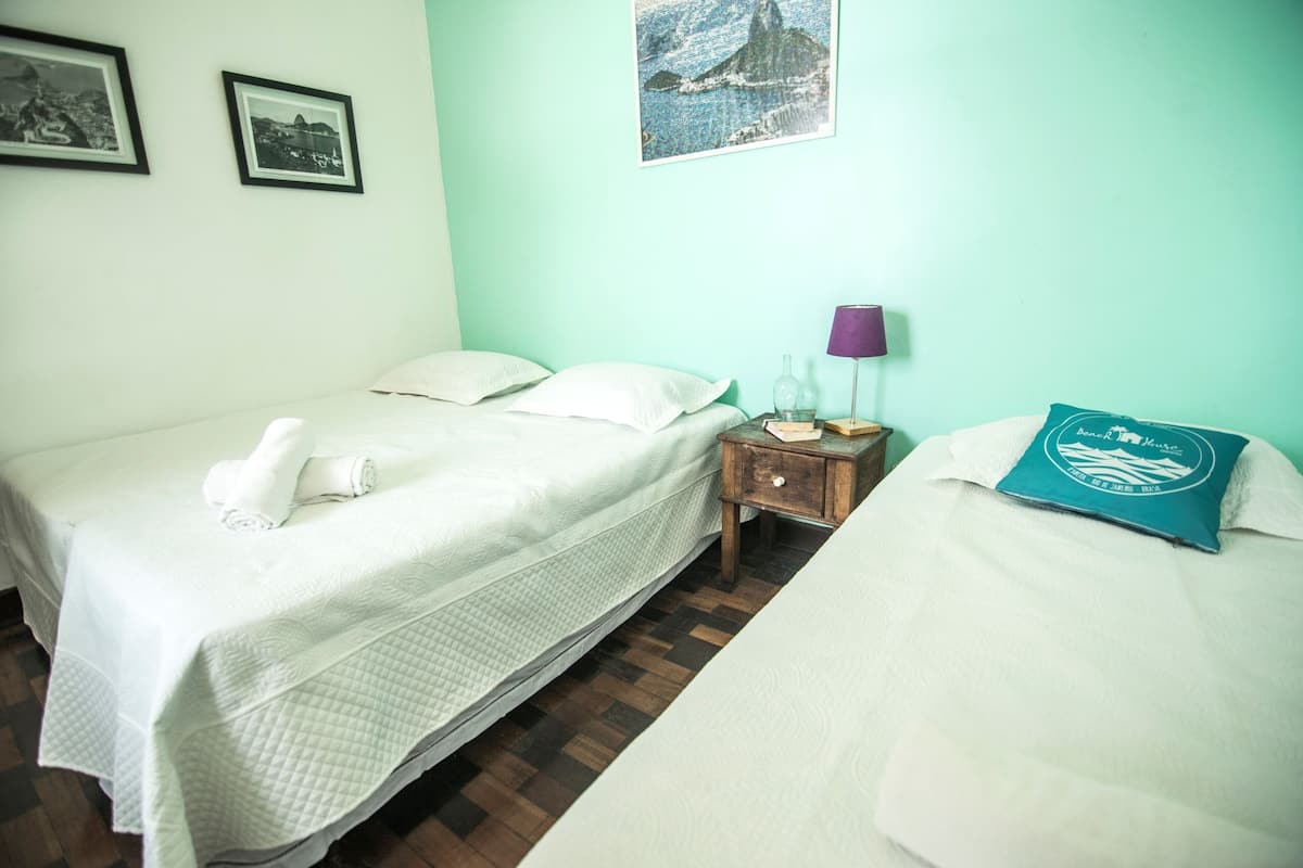 Quarto de hotel com duas camas, uma mesa de cabeceira com abajur e um quadro pendurado na parede.