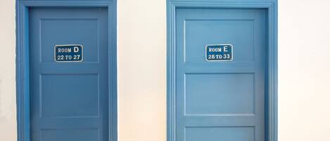 Dos puertas azules con las etiquetas 'ROOM D' y 'ROOM E', indicando los números de habitación '22 al 27' y '28 al 33' respectivamente.