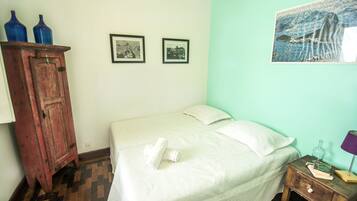 Quarto com cama, armário de madeira, duas molduras com fotos e uma mesa pequena com abajur.