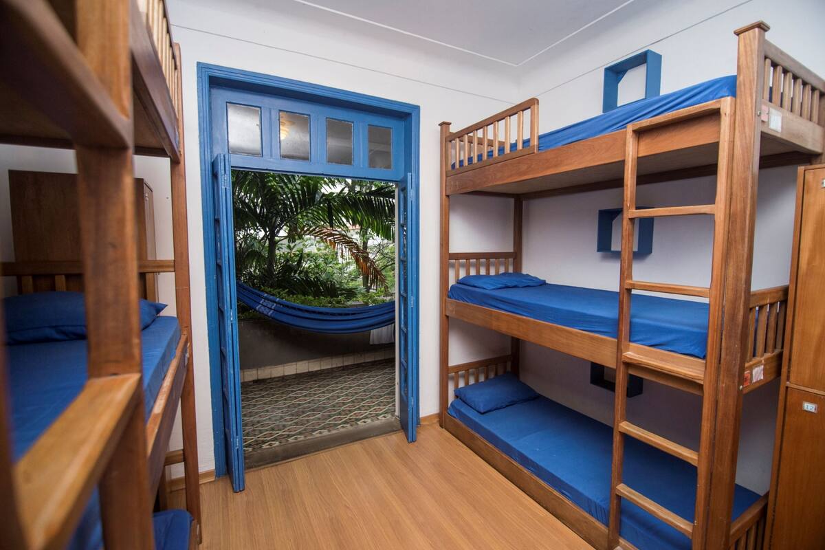 Quarto com beliches, uma rede e vista para o verde lá fora.