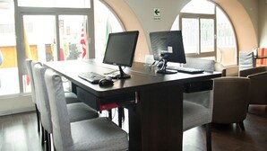 A conference room with two desks, each with a computer, keyboard, and mouse. There are four chairs around the desks. The room has large windows with arched tops and a door with a sign indicating an exit. - Best Western Trujillo (Trujillo)