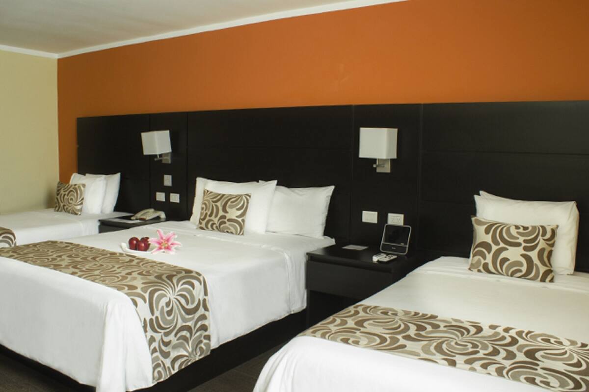 A hotel room with two beds, each with a patterned bedspread, a nightstand with a phone, and a wall-mounted lamp.