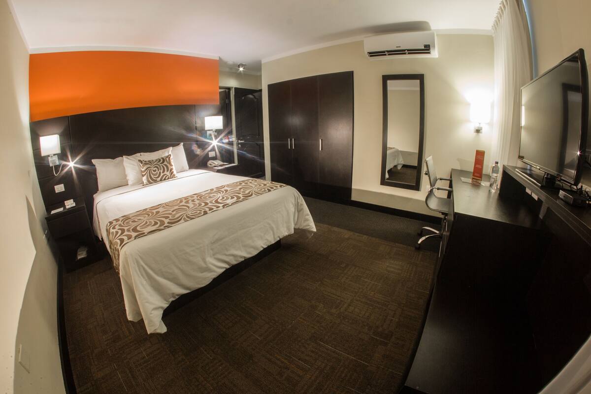 A hotel room with a large bed, a desk with a chair, a TV, and a wardrobe.