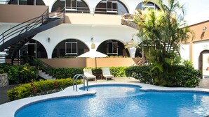 A swimming pool with a curved edge, surrounded by a white tiled deck. There are lounge chairs and a palm tree nearby. - Best Western Trujillo (Trujillo)