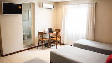 Quarto de hotel com duas camas, uma escrivaninha com um laptop, uma TV e um ar condicionado.