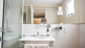 Un baño con cabina de ducha de vidrio, un lavamanos con espejo, un perchero para toallas y un secador de pelo montado en la pared.