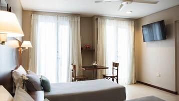 Een hotelkamer met twee bedden, een bureau, stoelen, een televisie en een plafondventilator.