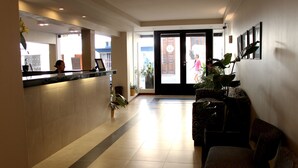 A hotel reception area with a reception desk, a waiting area with a sofa, and a large glass door leading outside. - Donsuites Apart Hotel (Corrientes)