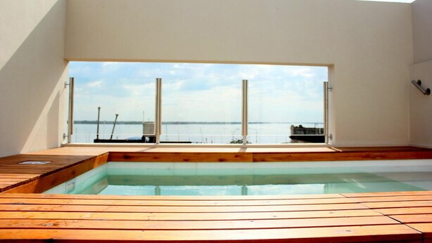 A modern indoor swimming pool with a wooden deck, large windows offering a view of the sea and boats. - Donsuites Apart Hotel (Corrientes)