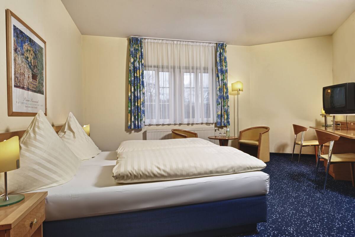 A hotel room with a bed, a desk, a chair, a television, and a window with curtains.