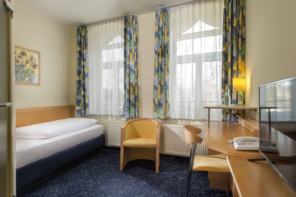 A hotel room with a bed, a desk with a telephone, a chair, and a radiator.