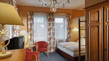 Ein Hotelzimmer mit einem Bett, einem Schreibtisch mit Lampe, einem Sessel, einem Fernseher und Vorhängen.