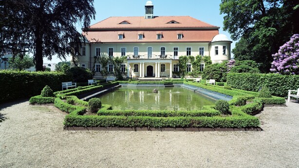 Un edificio grande con fachada simétrica, un patio central con fuente y jardines cuidados.