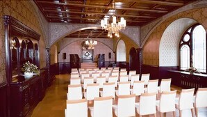 Un interior con hileras de sillas blancas dispuestas para un evento, techos abovedados y una araña.
