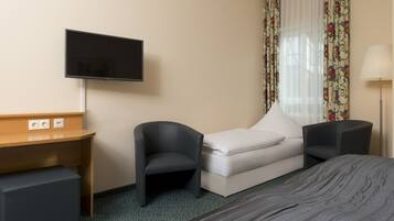 Habitación de hotel con cama, escritorio, silla, televisor y ventana con cortinas.