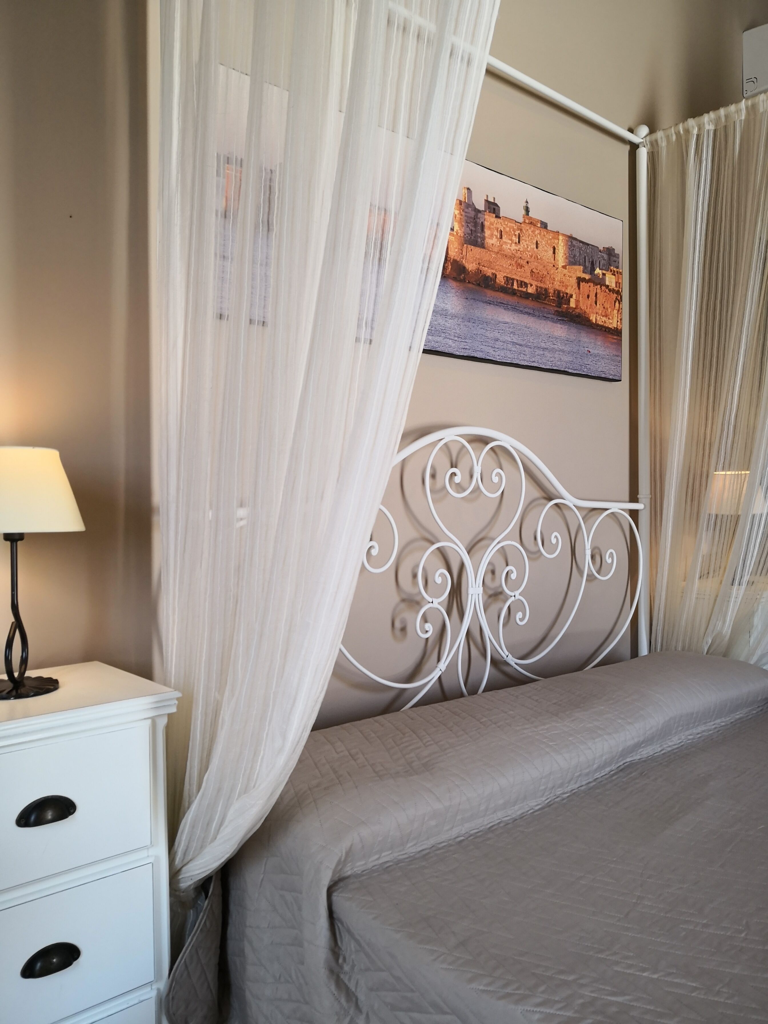 Une chambre à coucher bien rangée, avec un lit, une table de chevet dotée d’une lampe et un tableau accroché au mur.