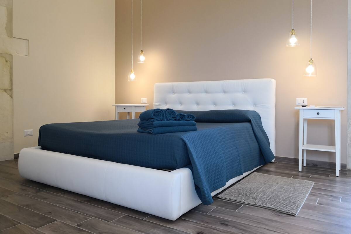 Un dormitorio con una cama, dos mesitas de noche e iluminación colgante.