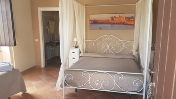 A bedroom with a bed, a nightstand, a bedside table, a wall-mounted TV, and a bathroom visible through an open door.