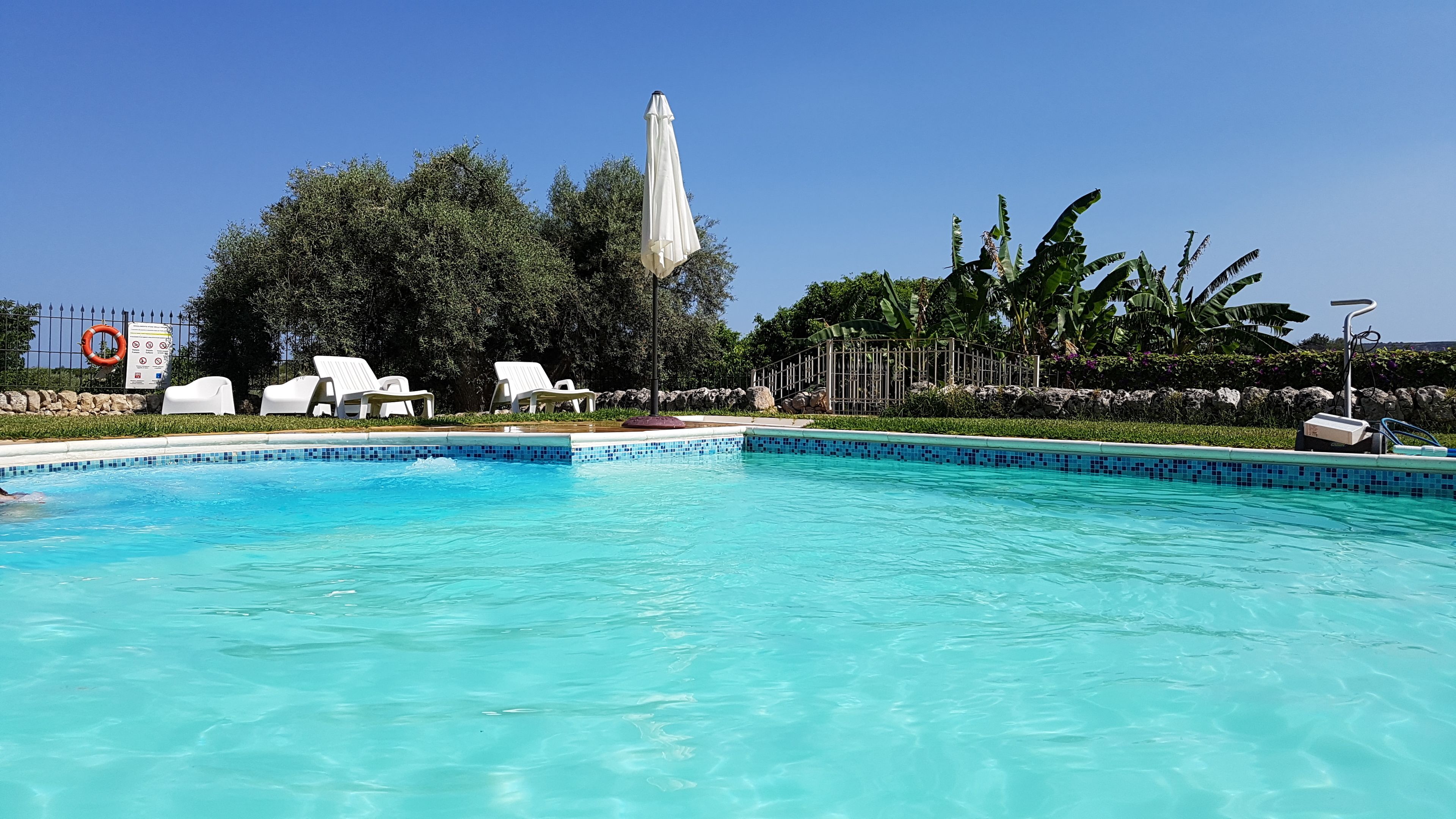 Une piscine à l’eau d’un bleu cristallin, entourée de chaises longues blanches et d’un mur en pierre.