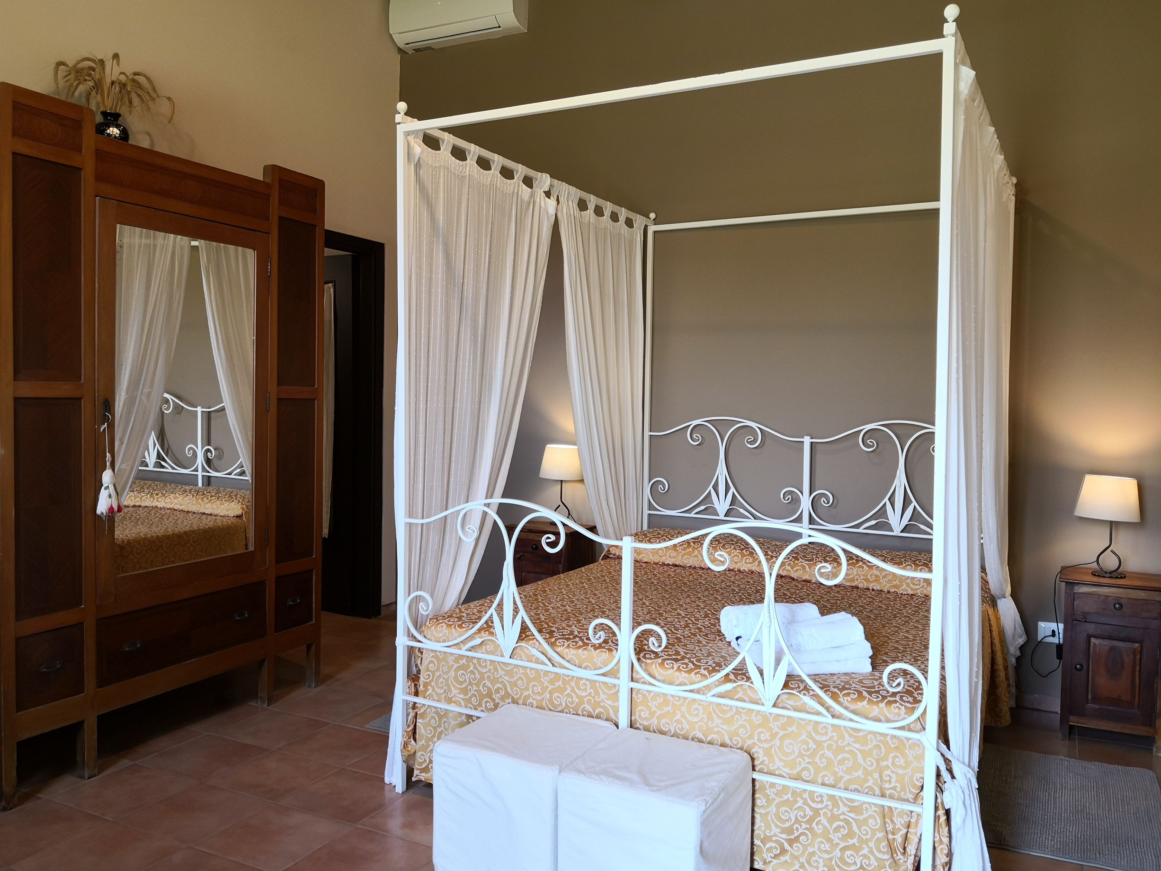 Una cama con dosel, una mesita de noche con lámpara y un armario de madera.