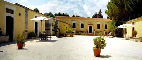 A courtyard with a building featuring a tiled roof, a table with chairs, and potted plants.
