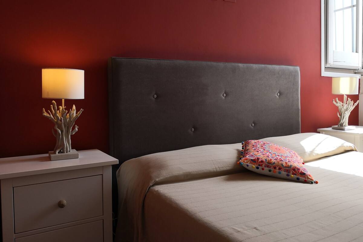 Un dormitorio con una cama grande, dos mesitas de noche y un ventanal.