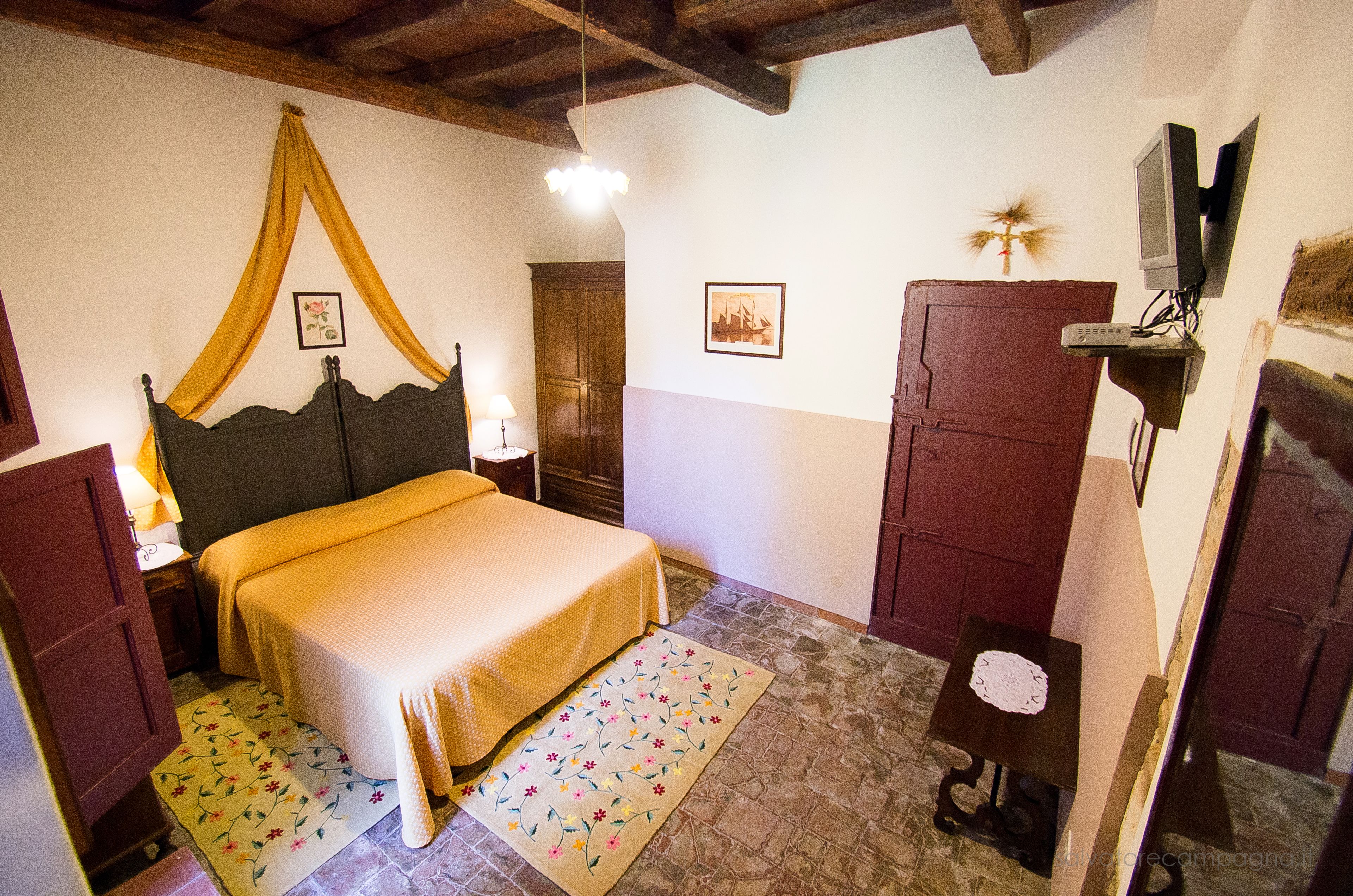 Une chambre à coucher comprenant un lit, une table de chevet, une lampe, une armoire et un téléviseur posé sur un meuble.