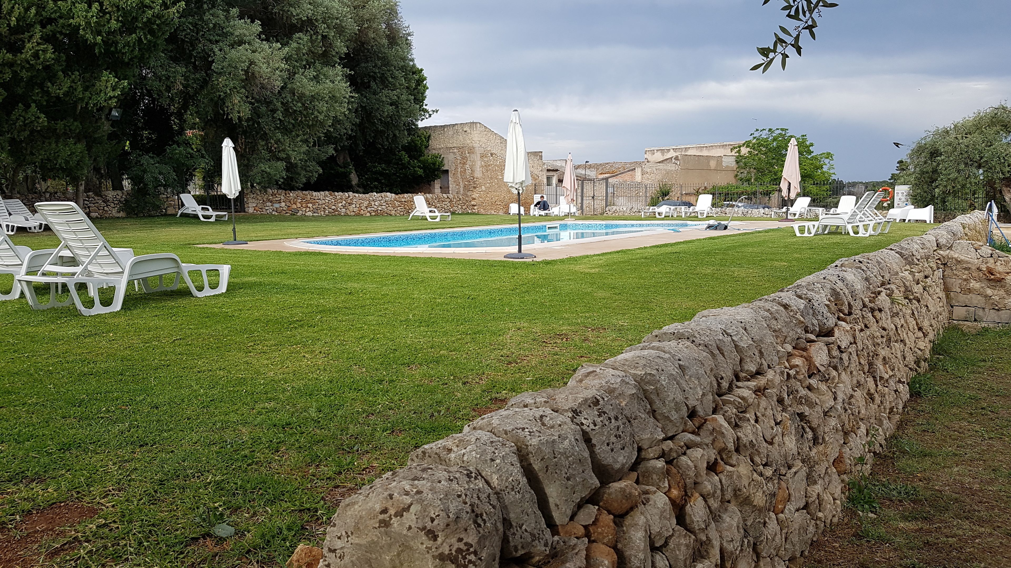 A pool area with lounge chairs and umbrellas, surrounded by stone walls and greenery.