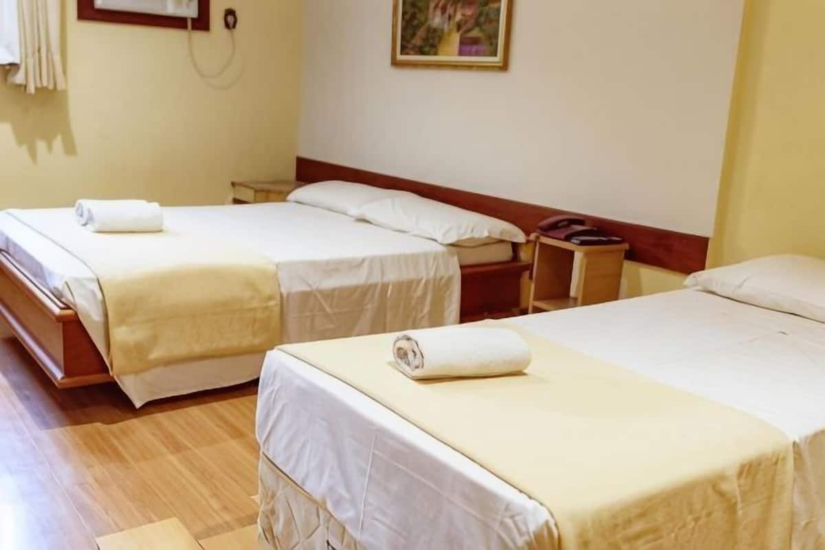 A hotel room with three beds, a wooden floor, a wall-mounted telephone, and a painting.