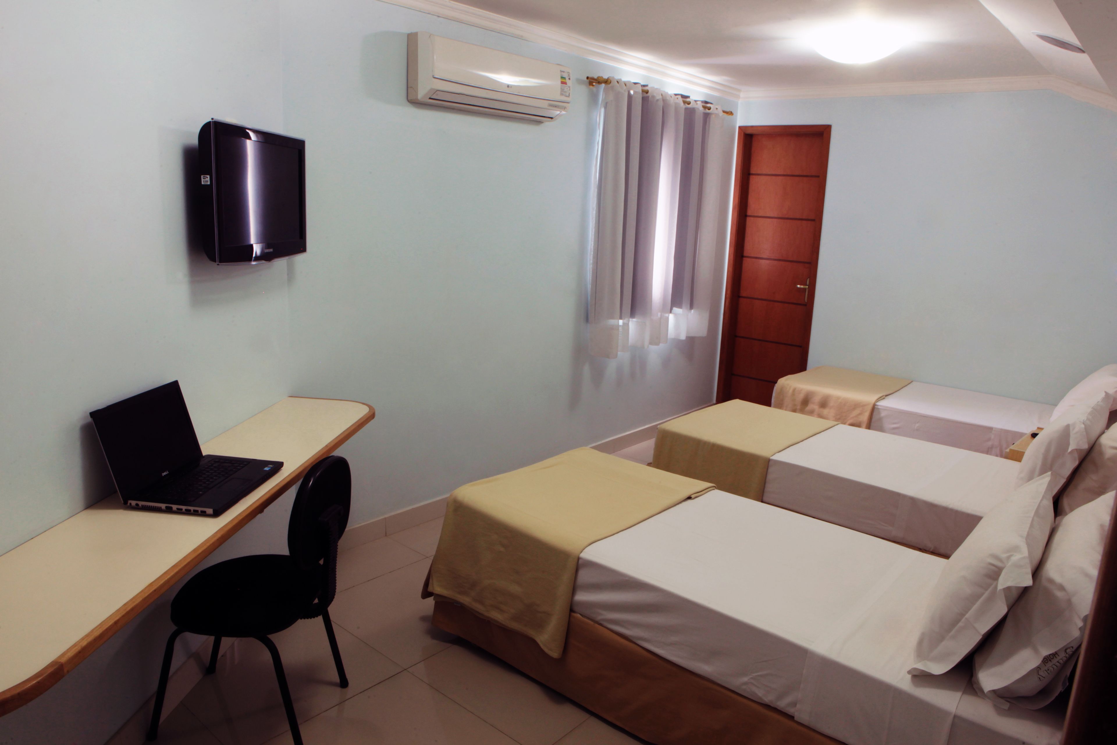 Una camera d'albergo con una scrivania, un portatile, una sedia, due letti, una TV e un condizionatore.