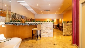 Un espace d’accueil d’hôtel comprenant un comptoir de réception en bois, une table basse en verre et un coin salon avec un fauteuil rembourré.