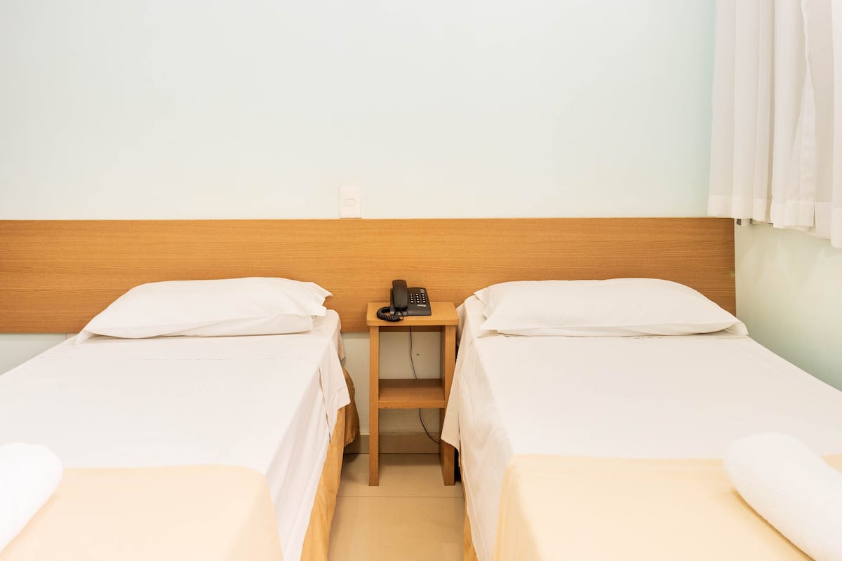 A hotel room with two single beds, a wooden nightstand with a telephone, and a light-colored wall.