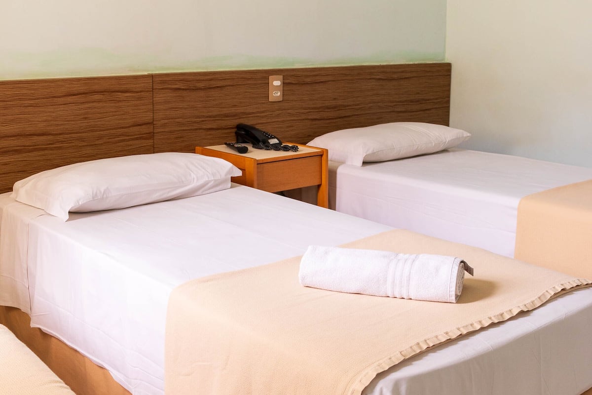 A hotel room with two single beds, a wooden headboard, a nightstand with a phone, and a beige blanket on one bed.