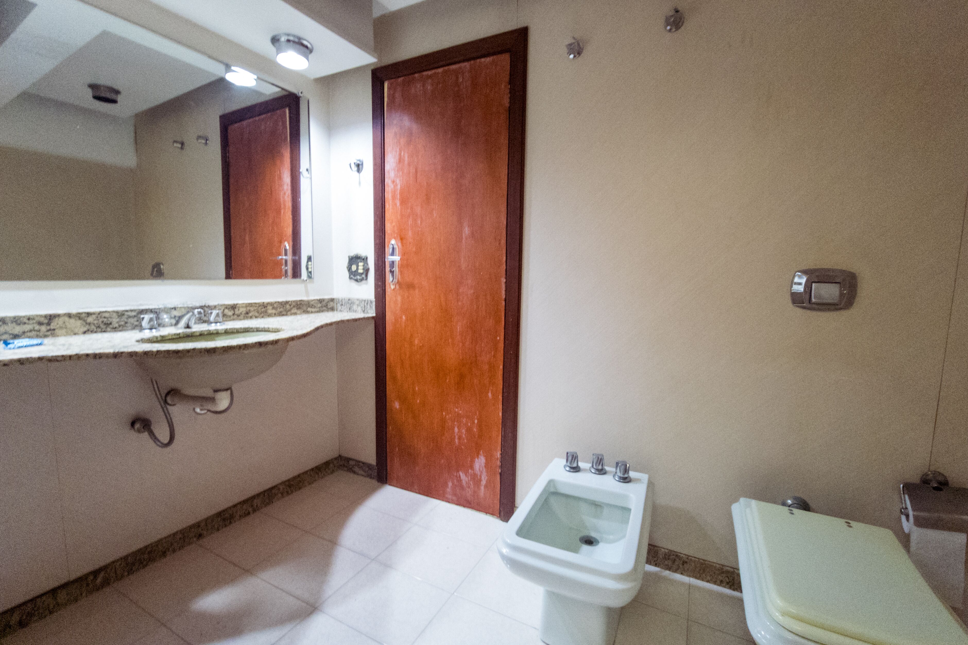 A bathroom with a sink, mirror, bidet, toilet, and a wooden door.
