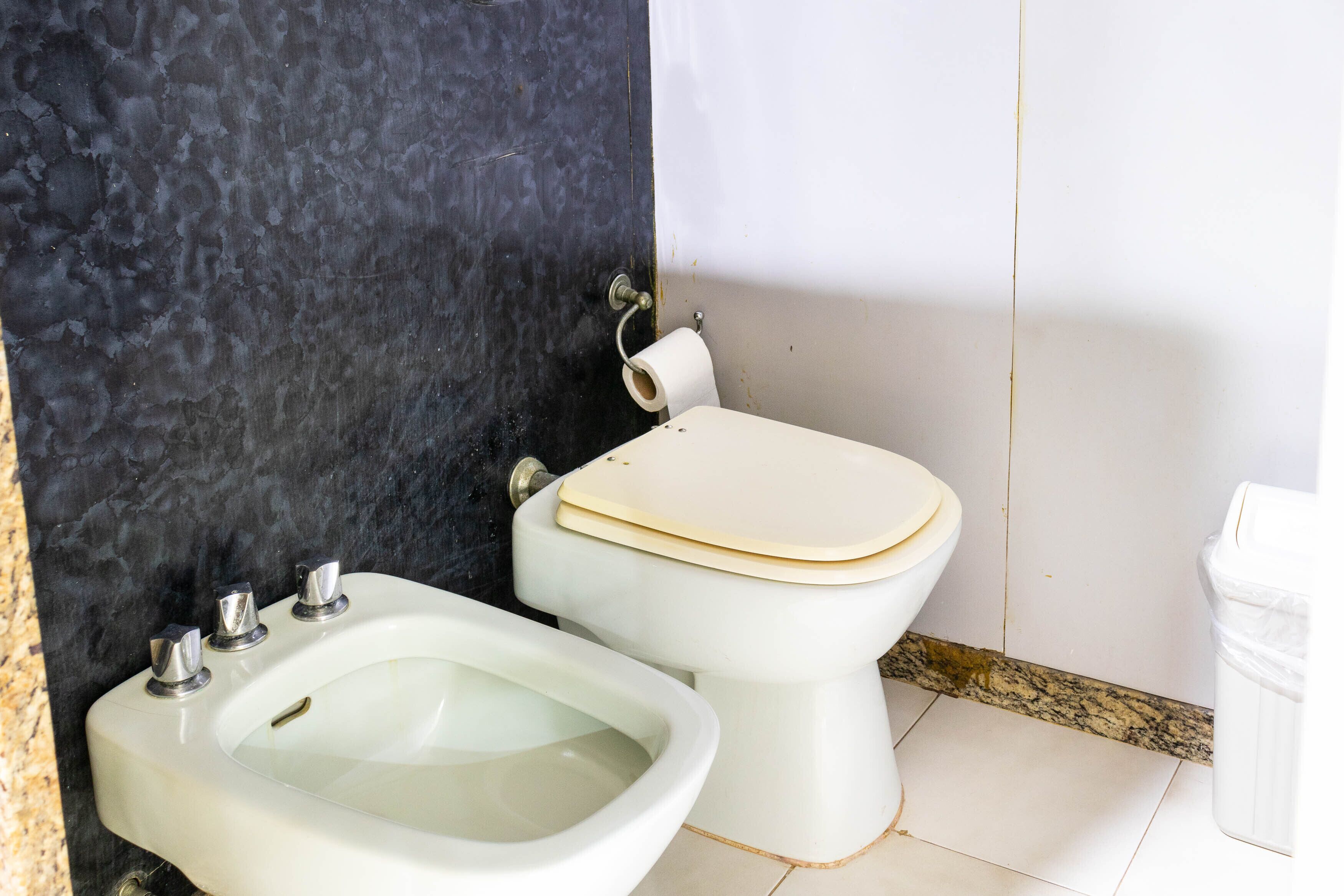 A bathroom with a bidet, toilet, and a marble wall.