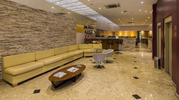 Un hall d’entrée moderne avec un mur en pierre, un canapé jaune, une table basse et un coin bar avec des bouteilles.