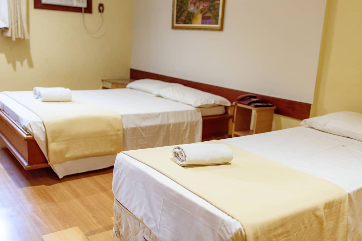 A hotel room with two beds, each with a white bedspread and a rolled towel on the bed. There is a wooden headboard, a nightstand with a phone, and a painting on the wall.