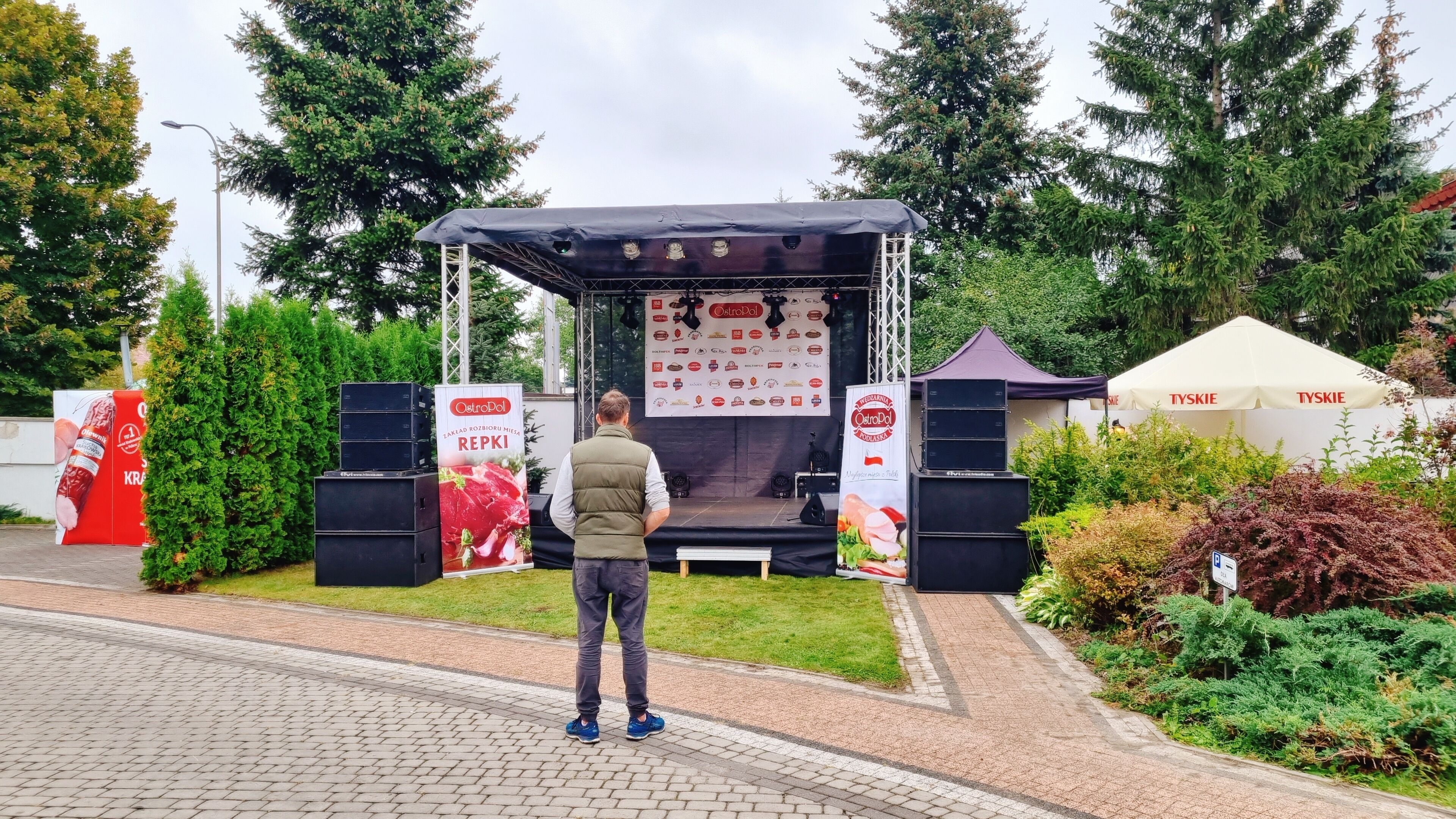 Un escenario con un cartel que muestra diversas marcas de alimentos, rodeado de follaje y una carpa.