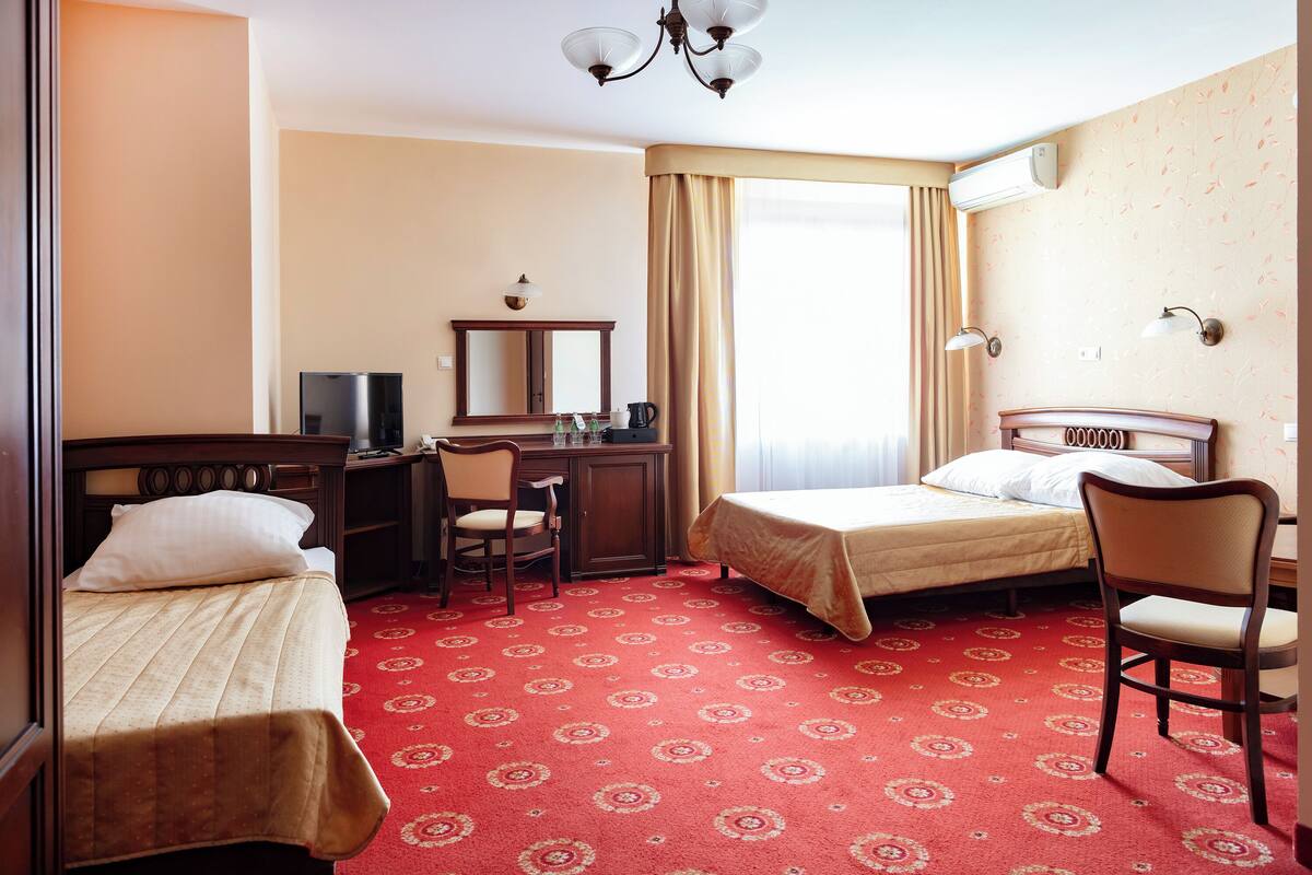 A hotel room with two beds, a desk, a chair, a TV, and a window with curtains.