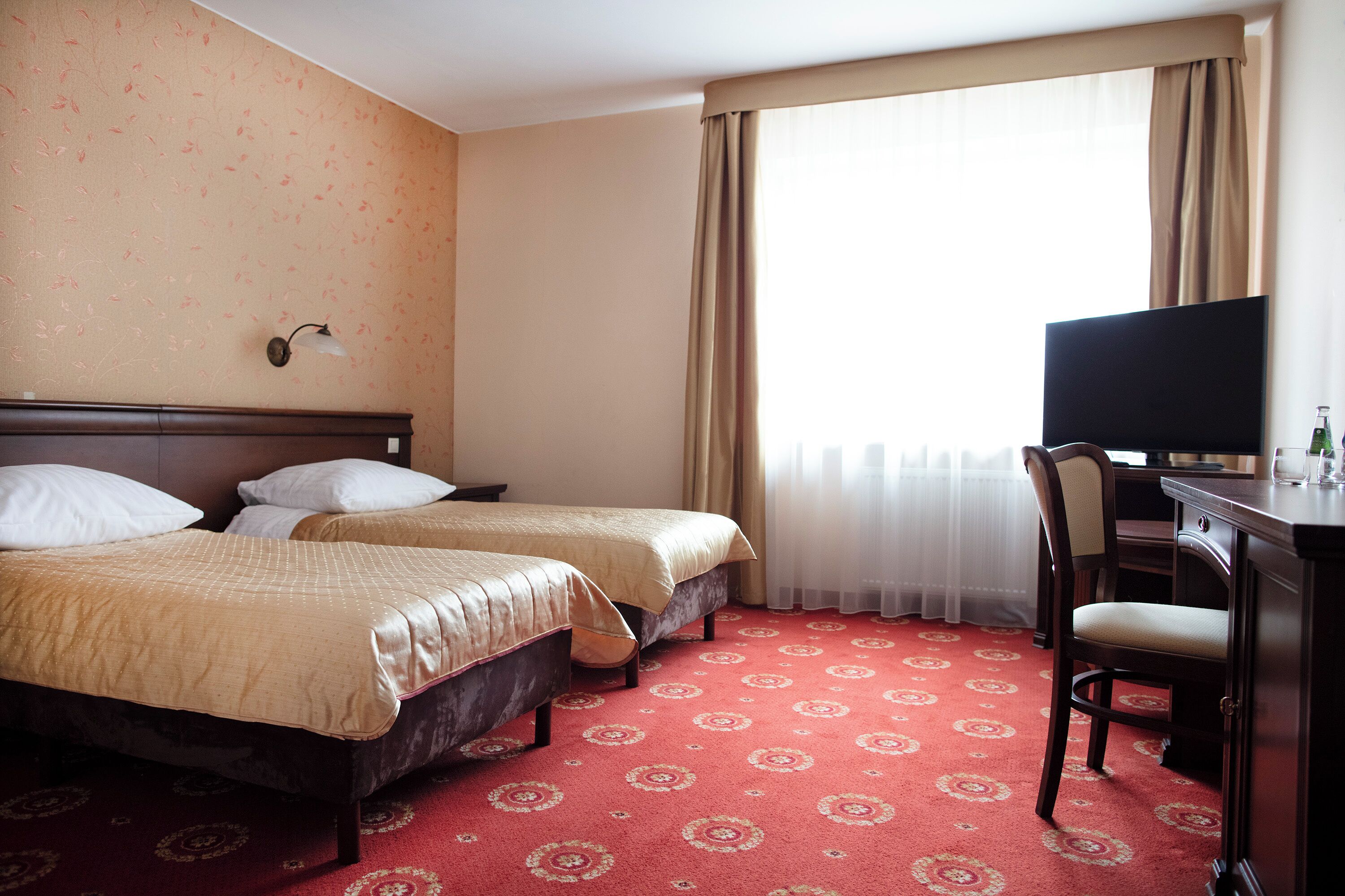 A hotel room with two beds, a desk, and a TV.