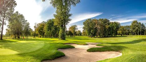 Un parcours de golf avec des bunkers de sable, des arbres et un ciel dégagé.