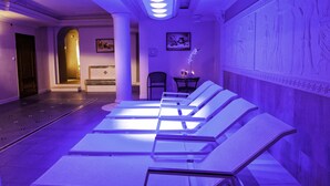 A room with a row of sunbeds under a purple-lit ceiling, a reception desk, and a wall with ancient carvings. - Anin Park Hotel (Warsaw)