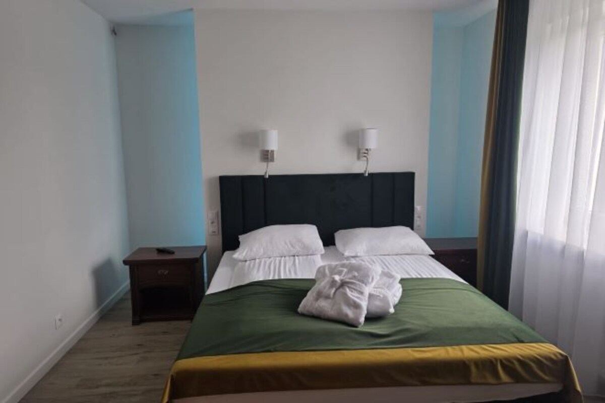 A hotel room with a bed, two bedside lamps, a nightstand, and a window with curtains.