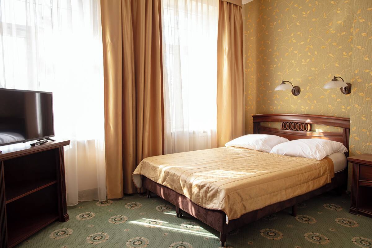 A hotel room with a bed, a television on a stand, and a nightstand.