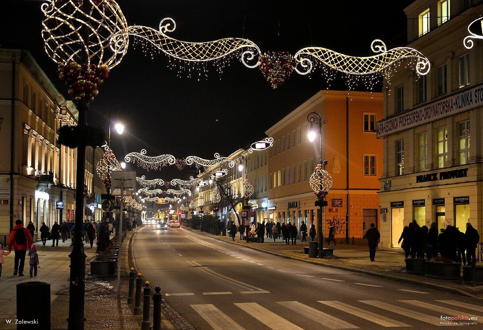 A street lined with buildings, decorated with string lights and spherical ornaments.